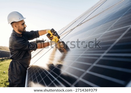 Yellow drill is in hands, installation process. Male solar engineer examining photovoltaic panels at a power station.
