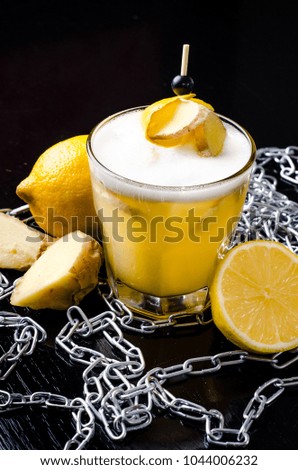 Yellow drink with lime, ginger, honey and ice. Organic strong cocktail in a glass with decoration root and berry, on black background. Bar alcohol menu, season.
