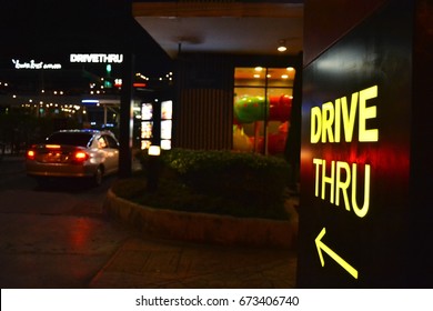 Yellow drive thru sign with an arrow pointer. A car drive into fast food restaurant in the late of night then order some food. Fast food store that open 24 hours selling burger, fried and nugget.