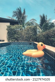 Yellow Duck Inflatable Ring Floating In Swimming Pool Surrounding With Palm Trees On Hot Sunny Summer Day At Backyard Of Modern Holiday House Or Luxury Villa. Vacation Concept