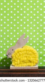 Yellow easter bunny in front of wall of points in a room. Bunny decoration and green wallpaper background on dots. Shadow of rabbit on the wall. Minimalist concept.