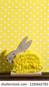 Yellow easter bunny in front of wall of points in a room. Bunny decoration and yellow wallpaper background on dots. Shadow of rabbit on the wall. Minimalist concept.
