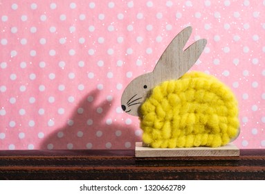Yellow easter bunny in front of wall of points in a room. Bunny decoration and pink wallpaper background on dots. Shadow of rabbit on the wall. Minimalist concept.