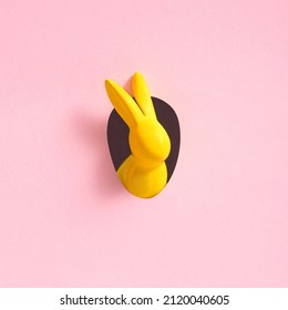 Yellow Easter bunny looks out an egg  shaped hole in the pink background wall  Abstract concept  Square and copy space 