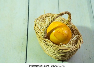 a yellow easter egg in a woven wooden basket on a straw pad, on light wooden floorboards, black and white photo