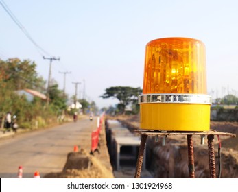 Yellow Emergency Lights Beside The Concrete Sewerage Construction Point And There Is A Red Fence Warning The Passer For Safety. With Road Background And Blue Sky Concept: Sewerage Construction.