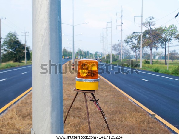 Yellow emergency lights beside metal poles on the\
middle of the road To send the yellow light signal warning to be\
aware of the danger of using the road On the asphalt road\
background and blue sky.