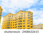 It is an yellow European apartment building in sunny midday. It is multicolored city buildig. There are clouds in a blue sky. It is close up view