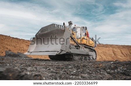 Yellow excavator in career moves overburden. Bulldozer combs the ground, with the bright sun and nice blue sky in the background
