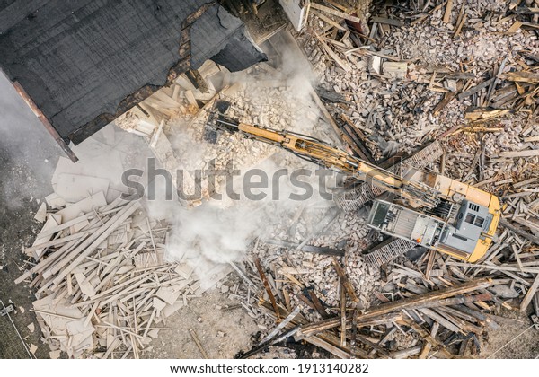 Yellow excavator\
destroys building. Heavy duty machine is demolishing a brick\
building. Demolition of the building . Demolition construction work\
aerial drone photo 