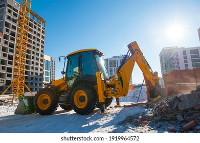 yellow excavator digs the ground at a construction site in winter against the background of a new house