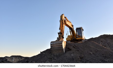 Yellow excavator during earthmoving at open pit on blue sky background. Construction machinery and earth-moving heavy equipment for excavation, loading, lifting and hauling of cargo on job sites