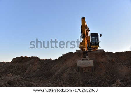 Yellow excavator during earthmoving at open pit on blue sky background. Construction machinery and earth-moving heavy equipment for excavation, loading, lifting and hauling of cargo on job sites