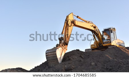 Yellow excavator during earthmoving at open pit on blue sky background. Construction machinery and earth-moving heavy equipment for excavation, loading, lifting and hauling of cargo on job sites