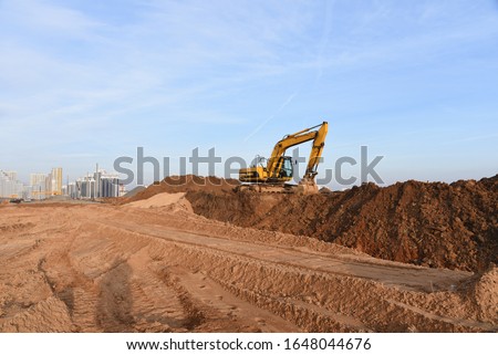 Yellow excavator during groundwork on construction site. Hydraulic backhoe on earthworks. Heavy equipment for demolition, construction and ground works. Digging foundation and laying storm sewer pipes