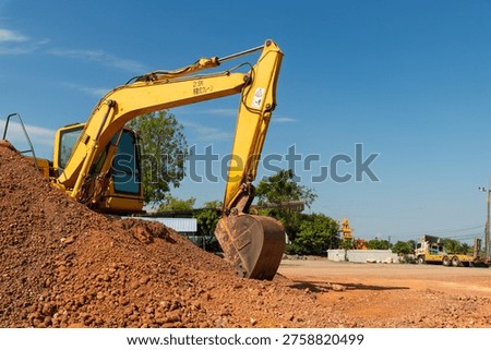 A yellow excavator efficiently digs through dirt at a construction site under a clear blue sky.