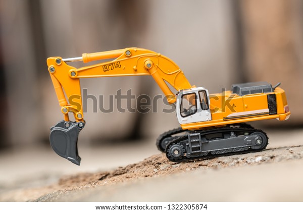 Yellow excavator model toy performs excavation work\
on a construction site.