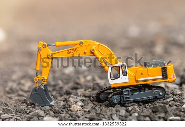 Yellow excavator model toy performs excavation\
work and load a gravel stone on a construction site. (Image\
stacking technique)
