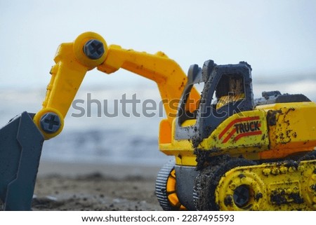The yellow excavator toy is placed on the beach after being played with a beautiful blurry blue sea background