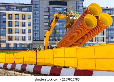 Yellow excavator transporting big orange pipes on the construction site before the modern building facade