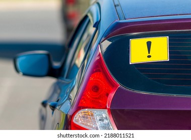 Yellow exclamation mark on the rear window of a car. Designation of an inexperienced driver behind the wheel, a warning signal. - Shutterstock ID 2188011521