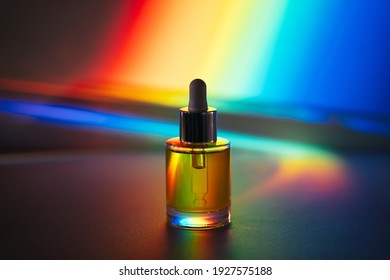 Yellow Face Oil With A Dropper Glass Bottle In Front Of Rainbow Prism Background. Side View