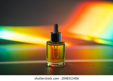 Yellow Face Oil With A Dropper Glass Bottle In Front Of Rainbow Prism Background. Side View