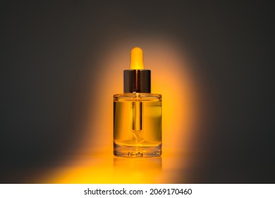 Yellow Face Oil In Glass Bottle With Dropper On Dark Background With Orange Spotlight