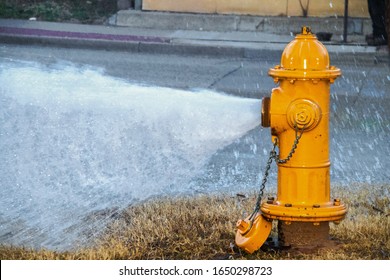 Yellow fire hydrant wide open gushing water onto the street with slightly grainy effect where water is falling back down over the pavement
