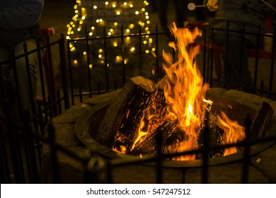 Yellow Firewood Fire In A Brick Fire Pit Dark Background With Little Christmas Light On Tree Truck 