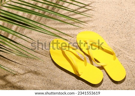 Yellow flip-flops with palm leaf on sand