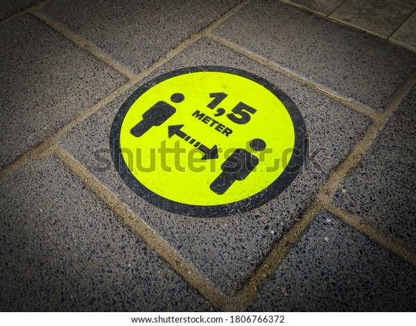 Yellow floor sticker on pavement which warns\
to keep 1.5 meters away from each other. Coronavirus measures and\
rules for social distancing. Close to shopping hall. Pandemic rules\
and prevention.