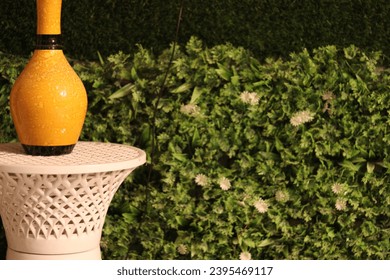 A yellow flower pot placed on a white stool beside with artificial grass and plant - Shutterstock ID 2395469117