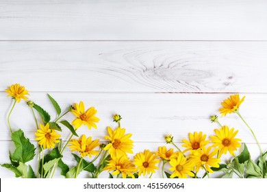 Yellow flowers on light wooden background. High top view.