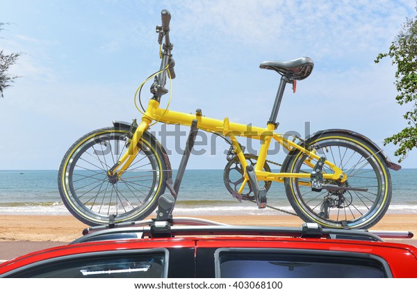 Yellow folding new bike on roof rack of red car\
Ready to depart tourist\
relaxing