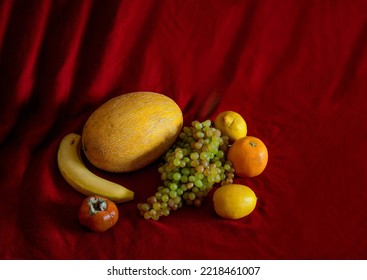Yellow Fruits ( mellow, banan, lemon and orange and green grapes and persimmon) on dark red background - Shutterstock ID 2218461007