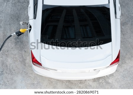 A yellow fuel nozzle is inserted into the gas tank of a white sedan on a concrete surface