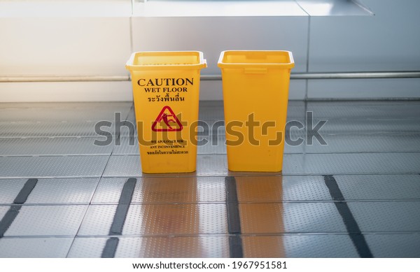 The yellow garbage bin and caution wet floor sign for\
the people . The Public trash on the side of the way to parking car\
in the airport 