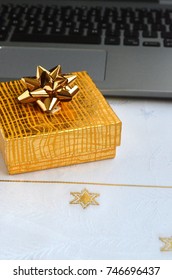 A Yellow Gift-wrapped Box With Gold Ribbon With A Laptop Computer Keyboard On A White Christmas Table Cloth - Secret Santa And Holidays At Work Concept