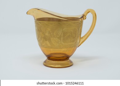 A yellow glass vintage creamer with engraved plating sits isolated on a white background.