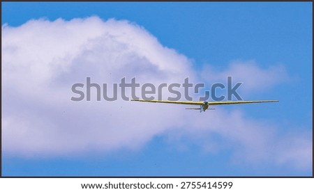 Yellow glider plane soaring through a bright blue sky with soft white clouds, captured from a distance during a graceful recreational flight on a sunny day.