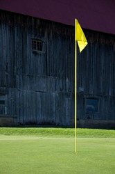 Yellow Golf Flag On Practice Green With Old Barn In Background Vertical