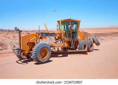 Yellow grader smooths dirt road in namib deserts - Road grader smoothing a dirt road in a rural area - Namibia, Africa