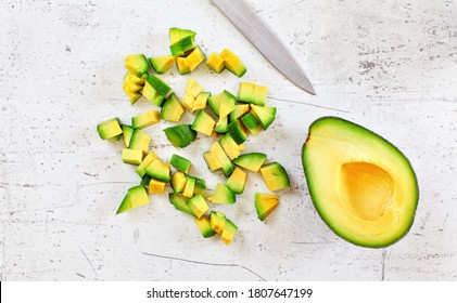 Yellow Green Avocado Pulp Cut To Small Pieces On White Stone Like Desk, Knife Blade Near, View From Above