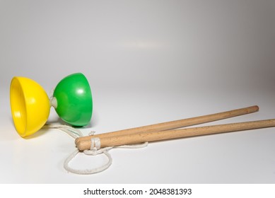 Yellow and green plastic diabolo with two wooden sticks and a white string ready to juggle on a white background