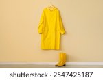 Yellow gumboots and raincoat on beige wall in hallway