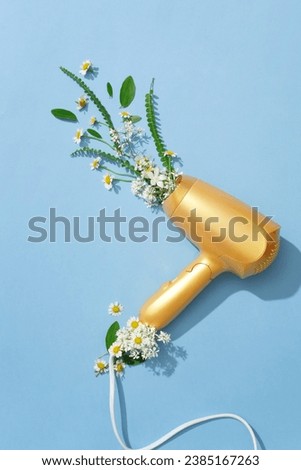 The yellow hair dryer is decorated with fresh daisies and green leaves on a pastel background. Creative images for advertising or other purposes. Top view.