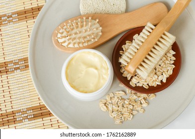 Yellow hair mask (banana face cream, shea butter facial mask, body butter) in the small white jar, oatmeal, massage body brush, wooden hairbrush. Natural skin and hair concept. Top view, copy space.