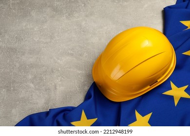 Yellow Hard Hat And Flag Of European Union On Light Grey Table, Above View. Space For Text