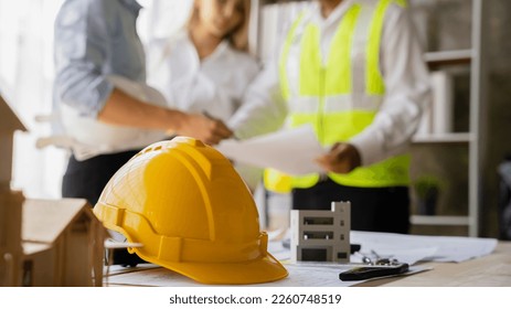 Yellow hard hat on workbench with Engineer teams meeting working together wear worker helmets hardhat on construction site. Asian industry professional team